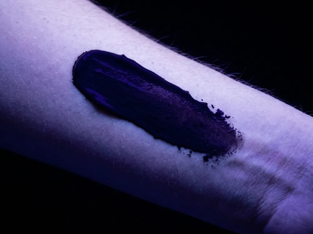 A forearm in violet black light with a smear of cream showing as a dark purple band with a ragged edge against the faintly glowing skin.