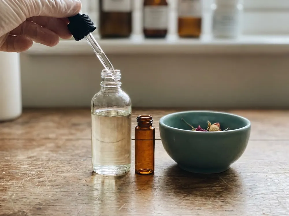 A dropper adding serum to a bottle beside a small amber vial and a bowl of dried botanicals, representing clinically studied dark spot ingredients