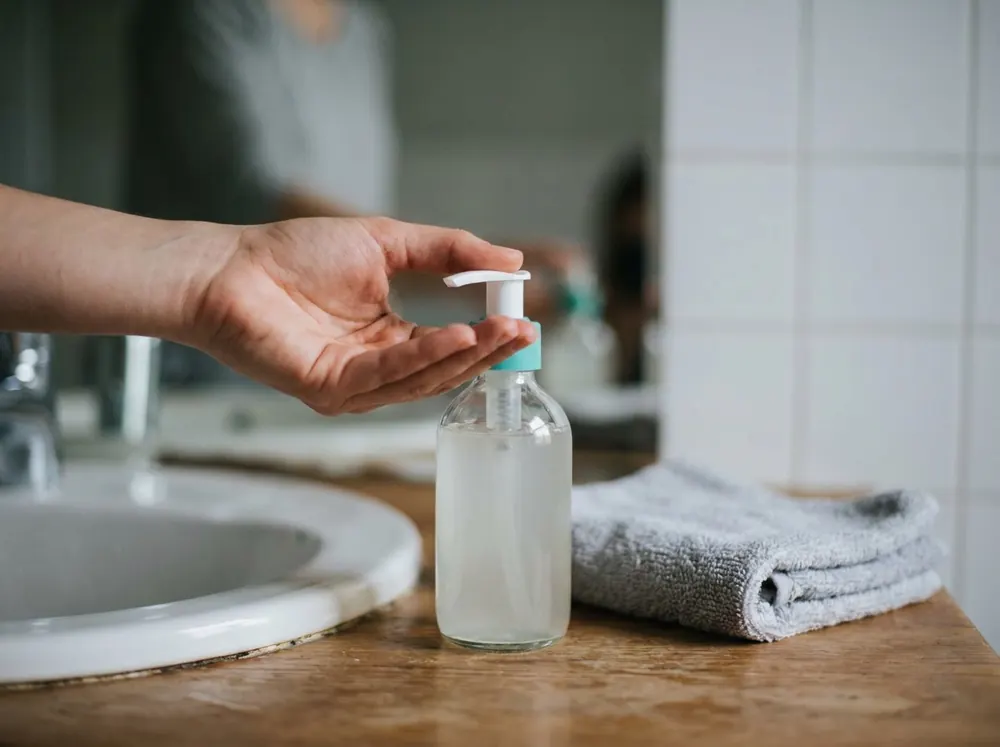 A hand pressing a foaming cleanser pump beside a folded towel over a bathroom sink