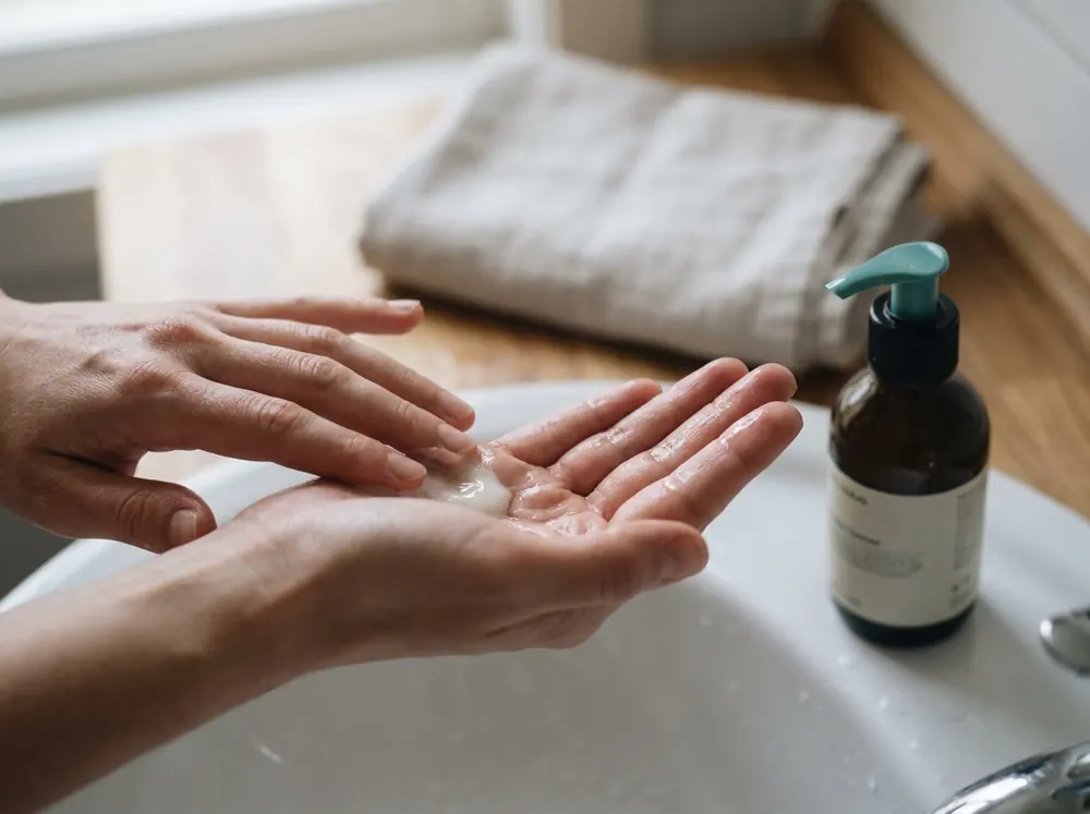 Washing the face with a foaming cleanser over a bathroom sink, the first step in a simple skincare routine