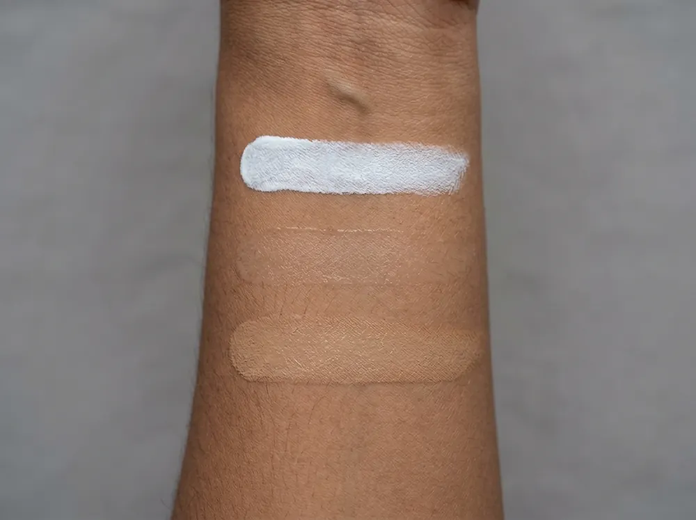 Three sunscreen textures swatched side by side on a forearm in flat daylight, one chalky, one clear, one tinted.