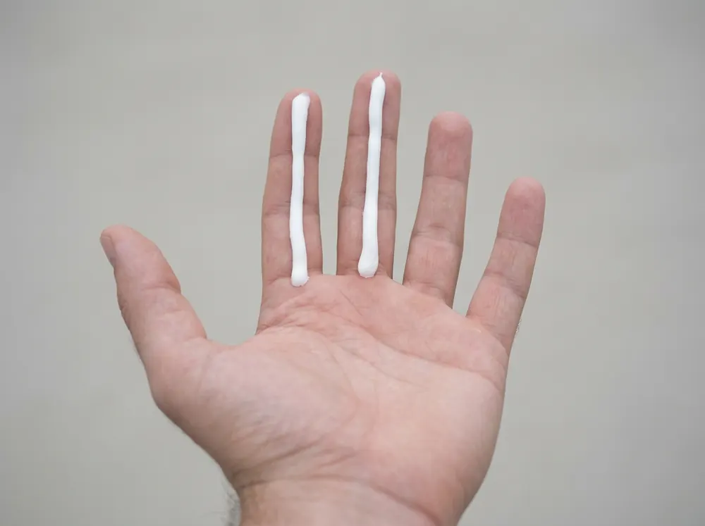 Two lines of sunscreen squeezed along the index and middle fingers of an upturned hand in flat daylight.