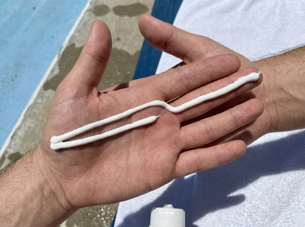 Sunscreen squeezed in two lines along the index and middle fingers of an upturned hand in bright sunlight.